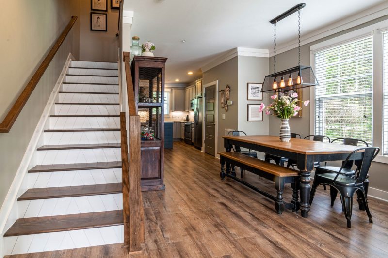 Bright and inviting dining area features a wooden table, staircase, and stylish interior lighting